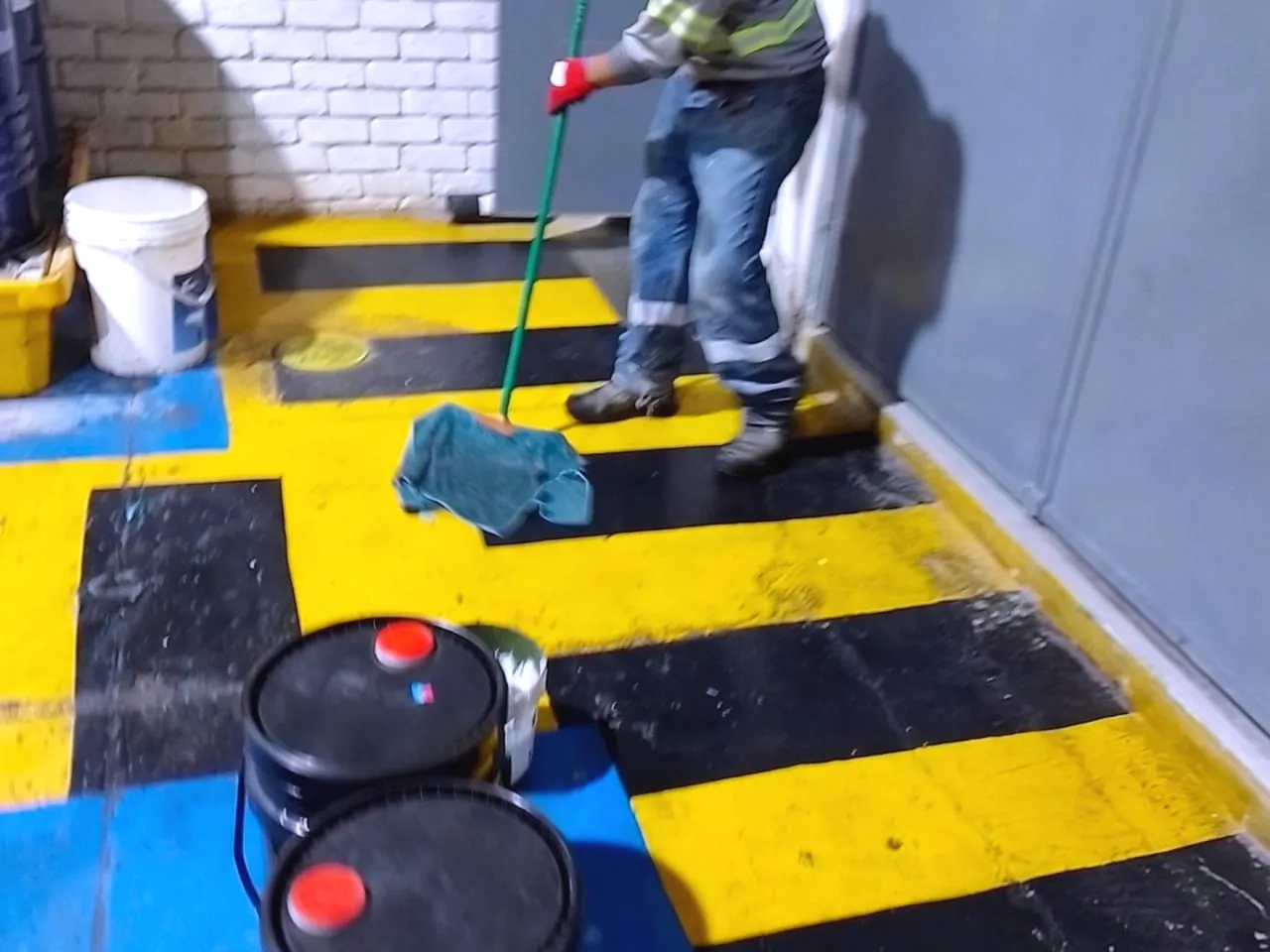 Operario pintando la demarcación amarilla y negra de una vía de circulación, con bolardos de protección ya instalados