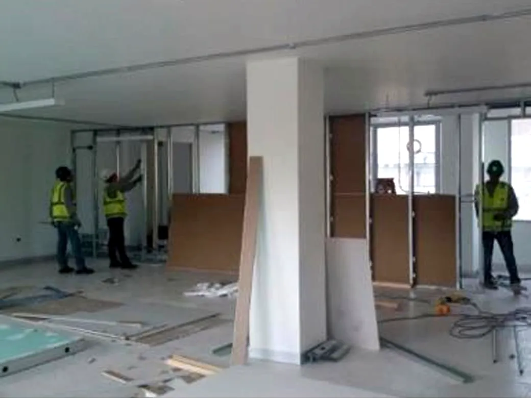 Oficina en obra con tabiquería y mamparas montadas, dos operarios trabajando en el ambiente