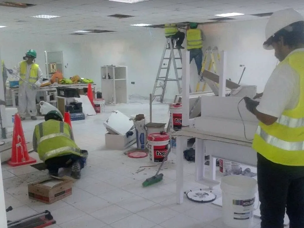 Local comercial en implementación: mobiliario blanco montado, escalera de trabajo y cuadrilla instalando el cielo raso