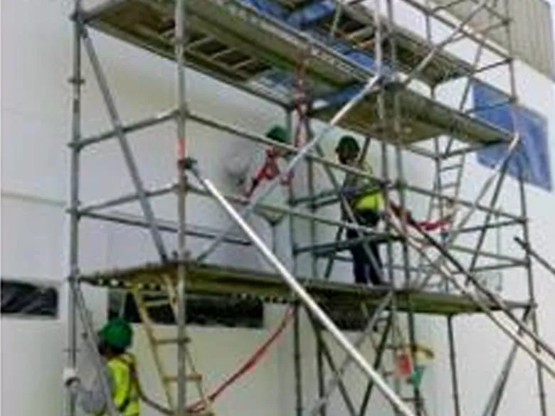 Cuadrilla trabajando en la fachada de una nave desde un andamio certificado de varios cuerpos