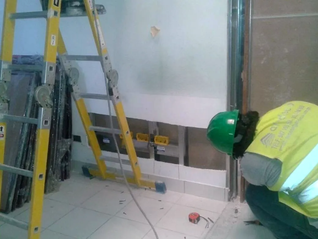 Operario instalando una mampara de vidrio templado, con los paños restantes apoyados junto a la escalera