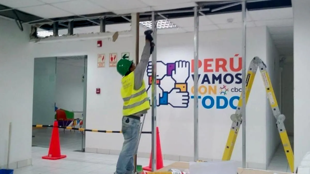 Operario colocando una luminaria en el cielo raso de una tienda ya rotulada, con conos de seguridad delimitando la zona de trabajo