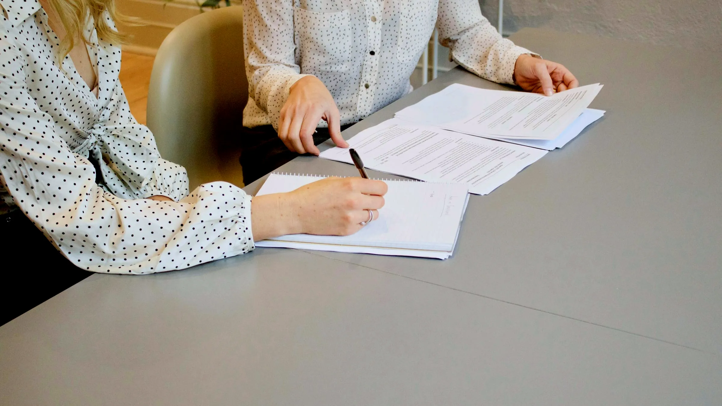 Dos personas firmando un juego de documentos sobre una mesa de reuniones