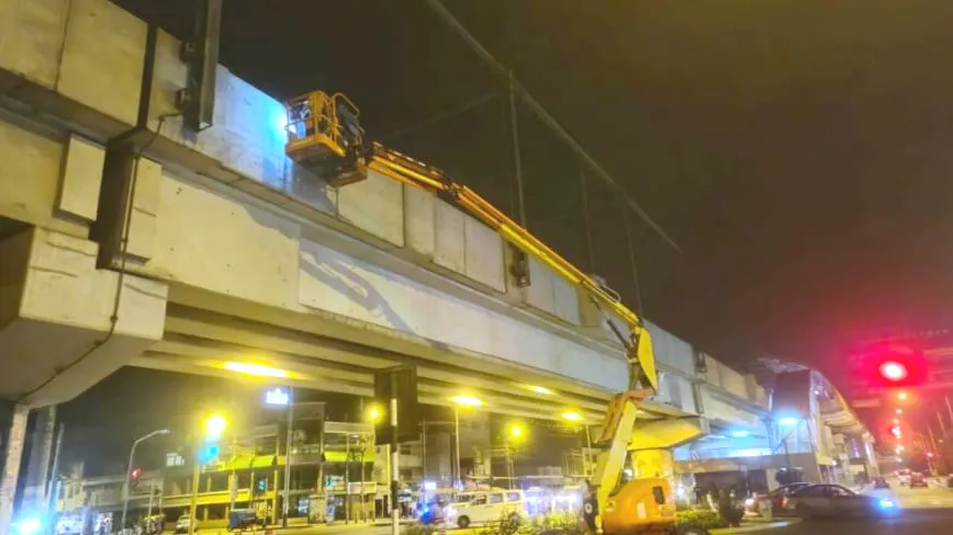 Grúa trabajando de noche bajo un viaducto, con la vía señalizada y en operación